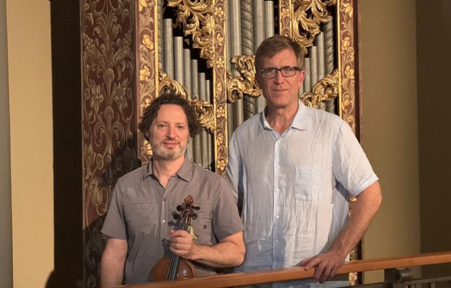 Martin Davids, holding a violin, stands alongside David Yearsley in front of an organ.