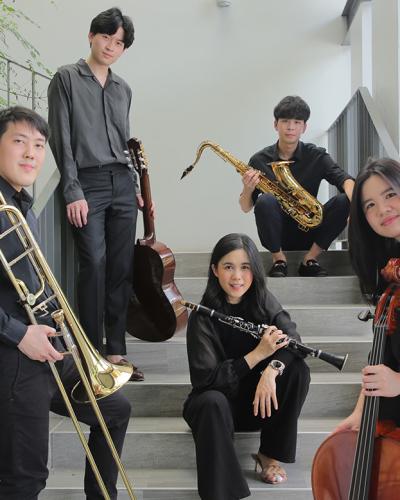 Five musicians wearing all black holding trombone, guitar, clarinet, saxophone, cello