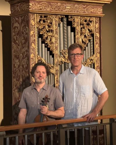 Martin Davids, holding a violin, stands alongside David Yearsley in front of an organ.