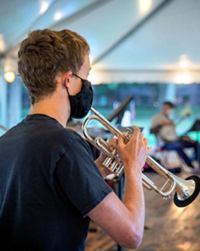 Student plays trumpet with a mask in a tent